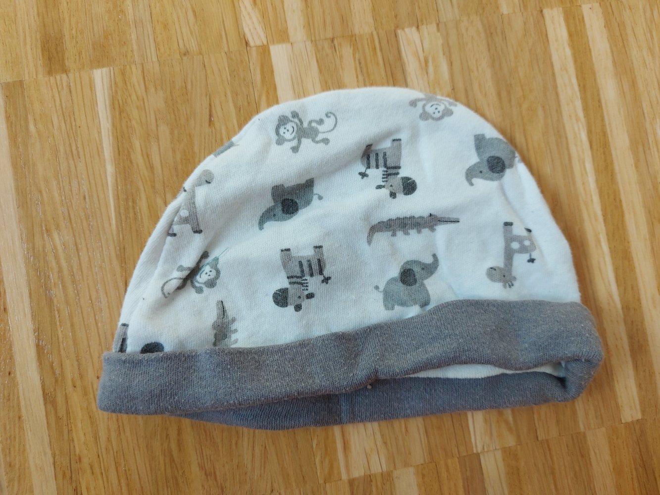 weiße Babymütze mit grauen Tiermotiven (Giraffe, Elefant, Affe usw.)